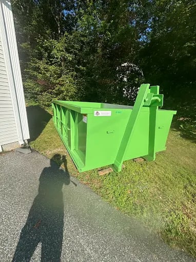 Large bright green dumpster sits on concrete near grassy lawn and trees